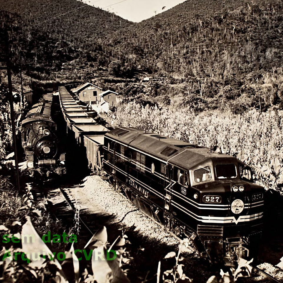 Locomotivas a diesel (B12) e a vapor conduzindo dois trens, lado a lado, em uma estação ferroviária da EFVM - Vitória a Minas, na década de 1950