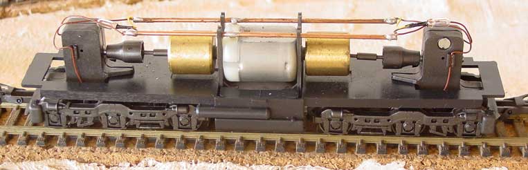Ferreomodelo de locomotiva Frateschi sem a casca, mostrando o motor, cardã de transmissão, truques redutores, volantes de inércia (flywheel), fiação e micro-lâmpadas, do alto