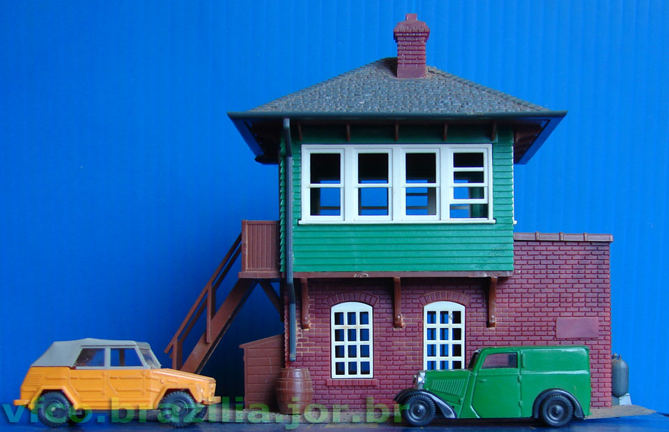 A cabine ferroviária Atlas juntamente com duas miniaturas de automóveis em escala HO (1:87) para maquetes de ferreomodelismo