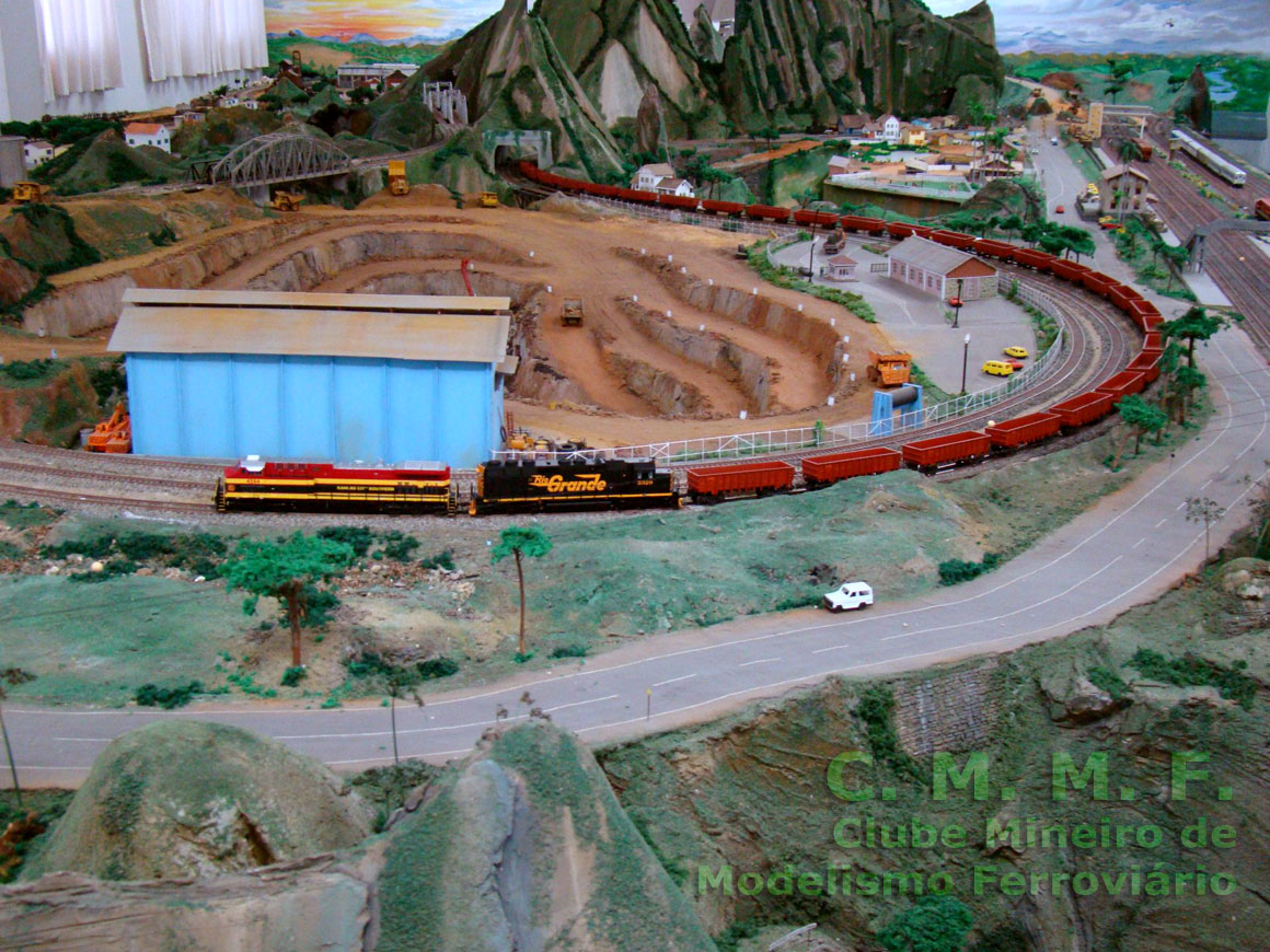 O longo trem, puxado por duas locomotivas, percorre os trilhos em torno da mina de ferro