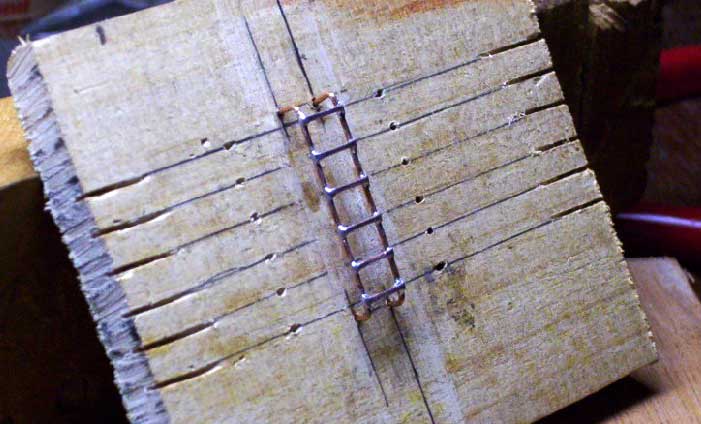 Tábua de madeira furada em intervalos regulares para servir de base à confecção das escadas em miniatura
