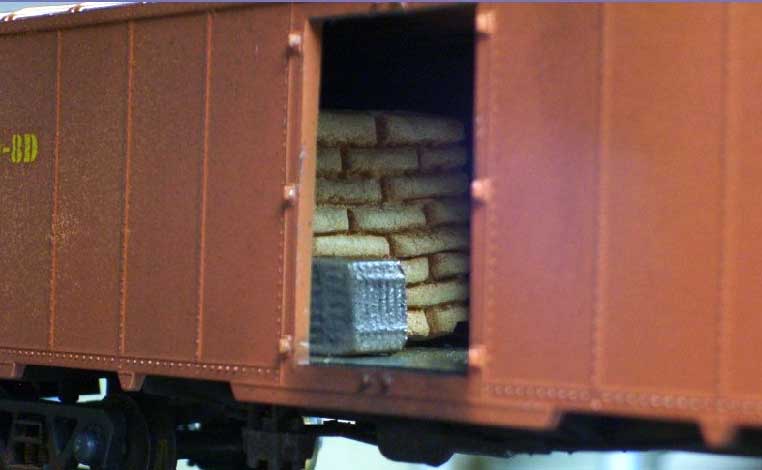 Aspecto do vagão em miniatura com a carga imitando sacos empilhados, visíveis através da porta aberta